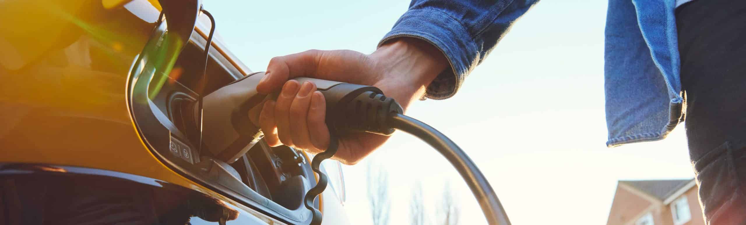 Person inserting an electrical vehicle charger into a yellow electric car